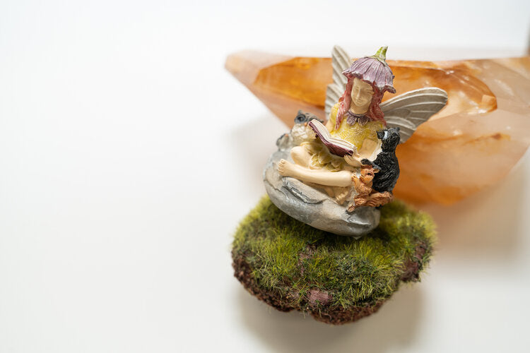 Small fairy reading book, sitting on grass, wearing a flower hat